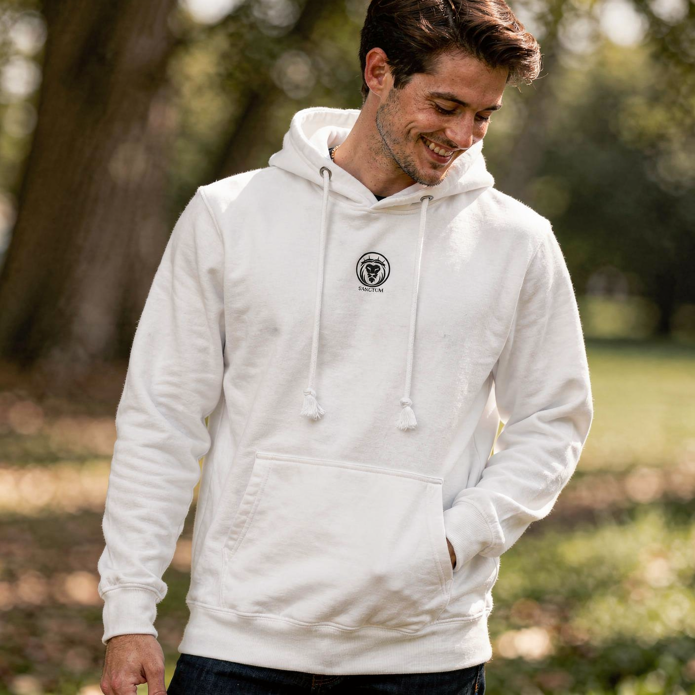 Man wearing a white hoodie with a logo in a park setting